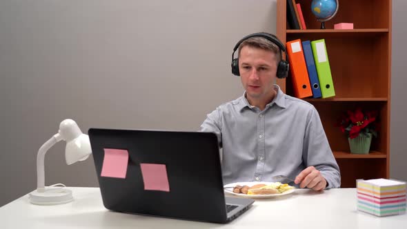 Freelancer in His Office Taking a Lunch Break and Eating While Doing a Video Call on His Laptop
