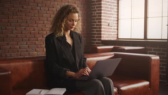 Young Stylish Businesswoman Working on a Laptop in a Loft Apartment with Red Brick Wall alt