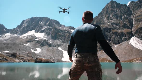 A young man with an athletic physique launches a drone from his hands near a mountain lake alt