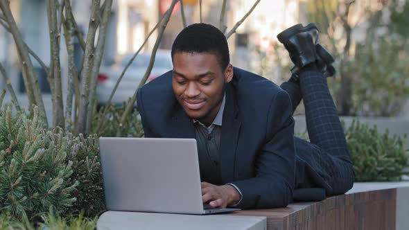 Young African American Businessman Typing on Laptop Laying on Her Stomach Outdoors Working Distantly alt