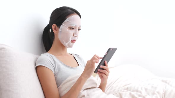 Woman Apply Facial Mask and Using Cellphone on Bed 