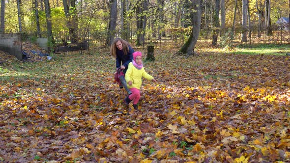 Mother and Little Daughter Have Fun with Garden Blower and Autumn Leaves in Yard