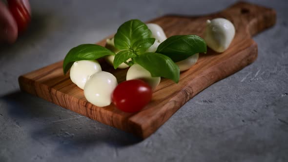 a hand puts the fresh tomatoes on a cutting board with mozzarella cheese alt