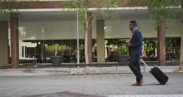 African american businessman with face mask walking with suitcase alt