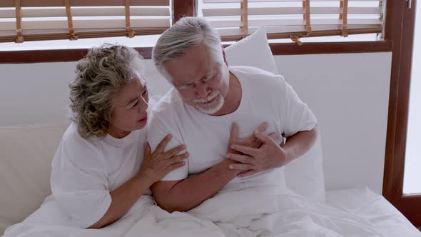 Asian elderly couple in bed, man's heart aches due to heart disease. alt