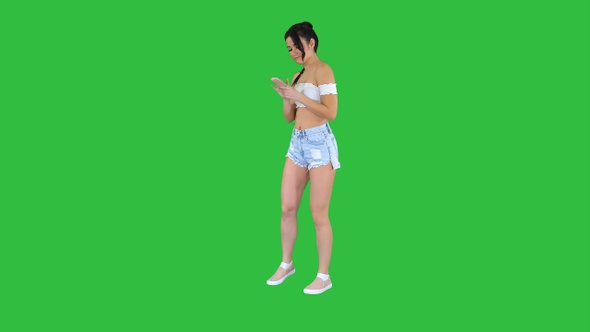 Cute girl checking her cell phone and dancing on a Green alt