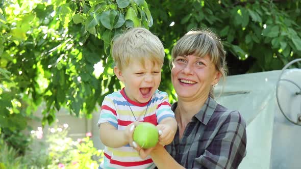 Mom and little son pluck a pear from a tree and want to eat.   Bright sunny day.