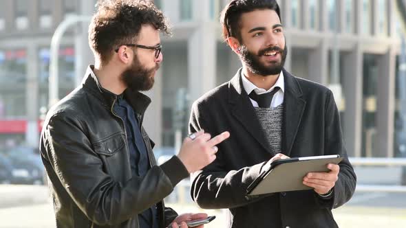 two young bearded contemporary businessman using tablet and discussing alt