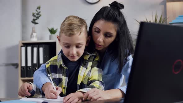 Young Dark Hair Woman Writing Something in the Notebook Together with Her Smiling Teen Boy alt