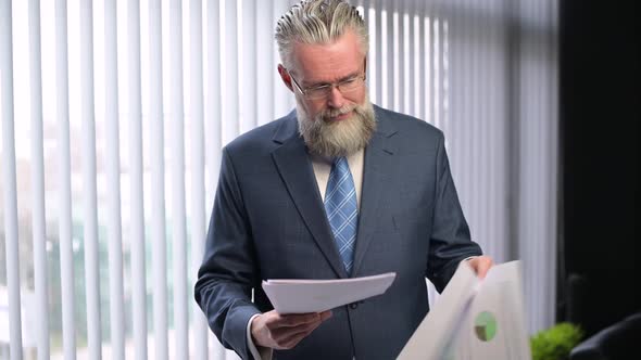 The mature gray-haired company executive examines the reports and shakes head alt