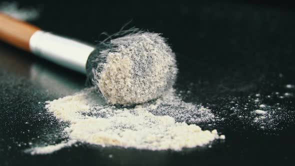 Cosmetic Powder for the Face is Poured From a Brush on a Black Background alt