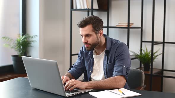 Excited Lucky Young Bearded Freelancer Sitting at the Desk with Laptop alt
