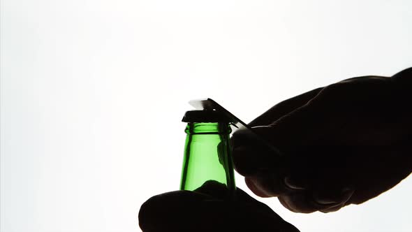The Silhouette of Male hands opening green beer bottle with opener