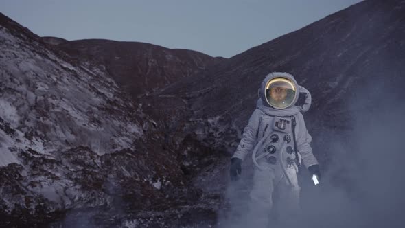 an Astronaut at Dusk with a Lantern Walks Down the Hill Through a Cloud of Steam alt