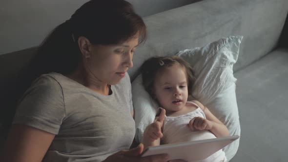 Mom and Little Daughter Are Lying in Bed with a Wake Cartoon on a Tablet. Mother and Baby Make Video alt