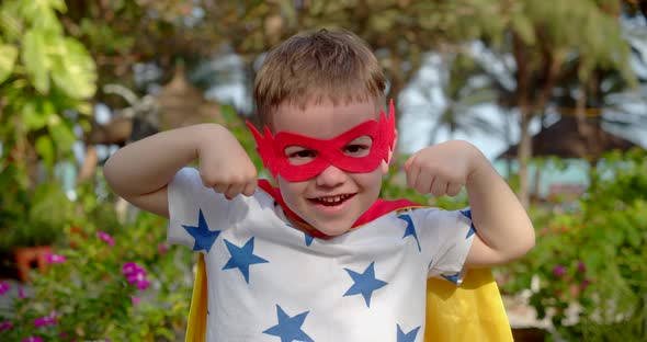 Portrait of a Cute Funny Child Boy in a Superhero Costume in a Red Cloak and Red Mask Plays a alt