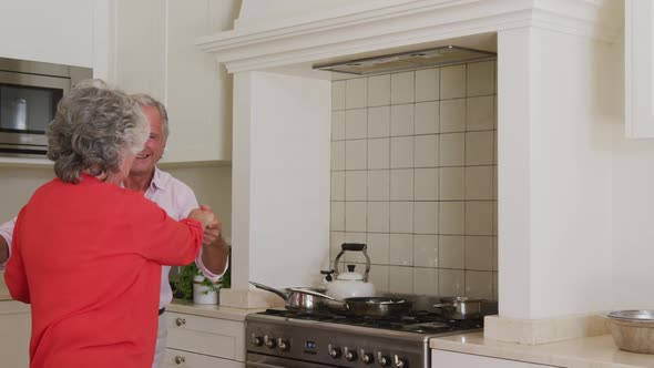 Happy caucasian senior couple having fun smiling and dancing in kitchen alt