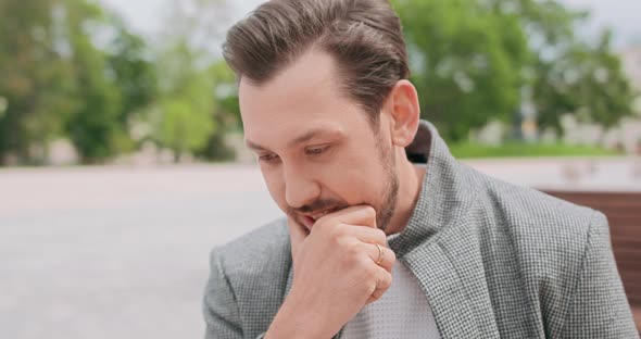 Close Up of Young Man with Mustaches and a Beard Sitting on Wooden Bench in the Square Typing on the alt