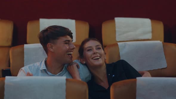 Attractive cheerful young caucasian couple laughing while watching film in movie theater. alt