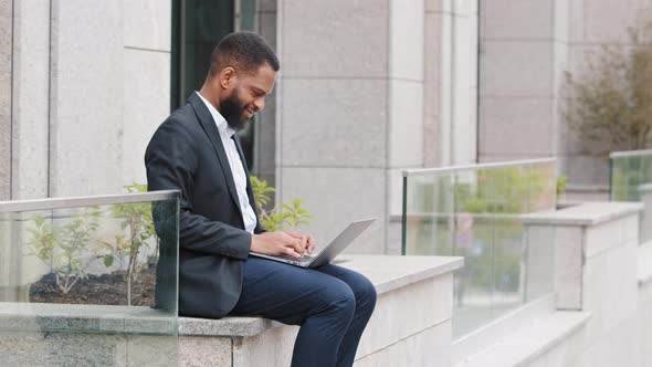 Serious Bearded Young Mixed Race Man Using Laptop Keeps on His Knees Notebook Sit Outdoors with alt