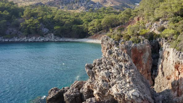 Flight along rocky cliff edge reveal idyllic Turkish azure blue water bay; drone alt