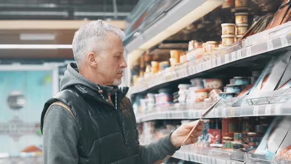 In the Supermarket An Elderly Grayhaired Man with a Beard Chooses Food in the Fish Department of the