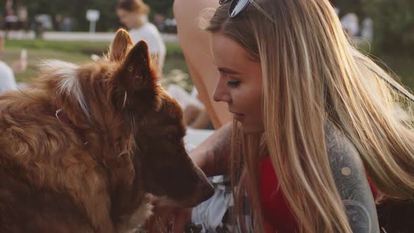 Younng Woman Petting Her Border Collie Dog While Sitting on Grass in Park