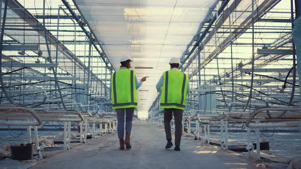 Two Factory Employees Walking in Empty Greenhouse Discussing Production Level alt
