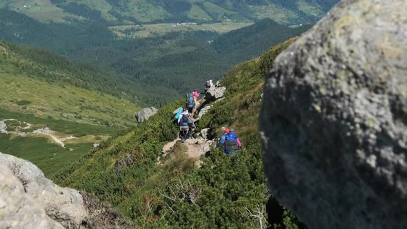 Group of Tourists and Children with Backpacks Go Down on Stone Trail in Mountain alt