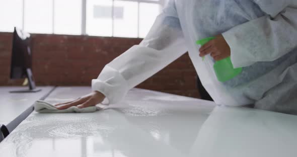 Midsection of cleaner wearing protective overalls disinfecting office and furniture alt