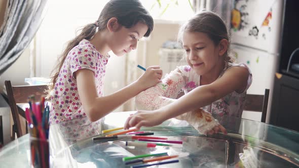 Caring Child Paints with a Bright Color a Plastered Hand To His Sister alt