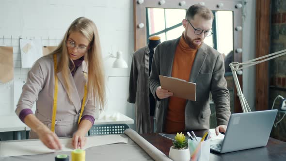 Male and Female Colleagues Dressmakers Choosing Material for New Garment Working Together Using alt