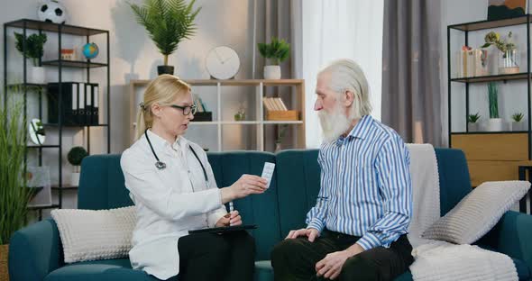 Doctor Giving Tablets to Her Old Male Patient and Telling How to Take them During Home Visit alt