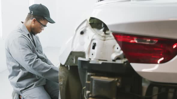 African American male car mechanic kneeling by a car and repairing it alt