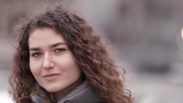 Closeup Portrait of a Young Woman with Curly Hair Posing on a City Street Wearing a Jacket Cold alt