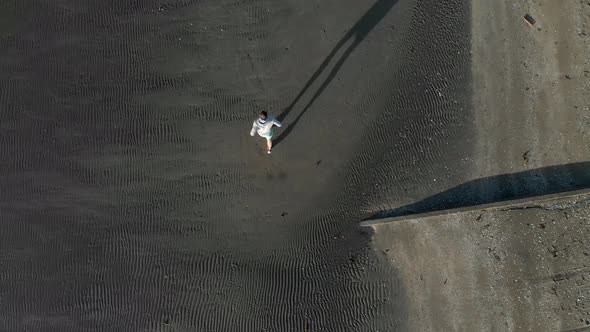Aerial tilt up shot of young man running on a beach in Auckland, New Zealand alt