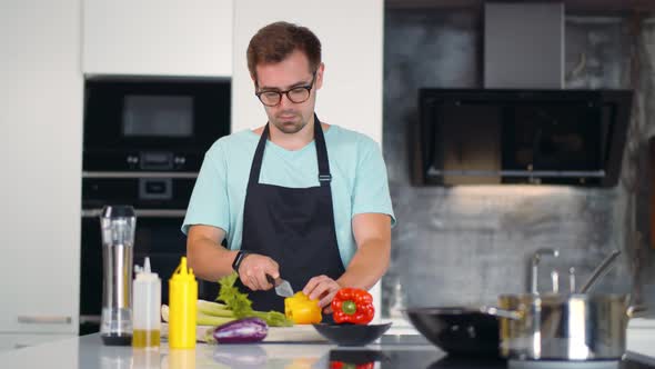 Cheerful Young Man in Apron Preparing Healthy Meal with Vegetables in Kitchen. alt