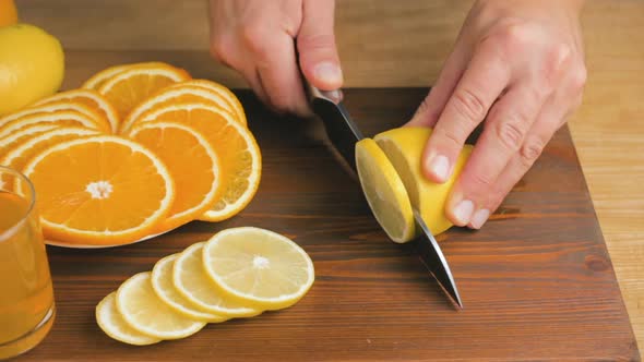 Male hand with big knife slicing lemon citrus fruit on the cutting board at kitchen