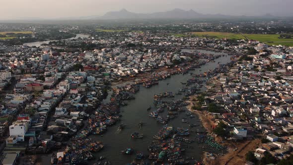 Southeast Asian local fishing village with many boats sailing dirty river at sunset alt