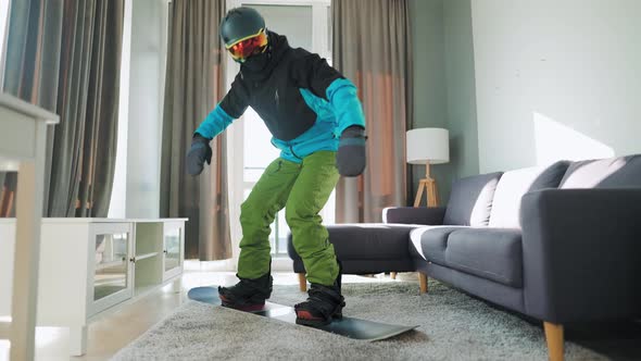 Fun Video. Man Dressed As a Snowboarder Rides a Snowboard on a Carpet in a Cozy Room. Waiting for a alt