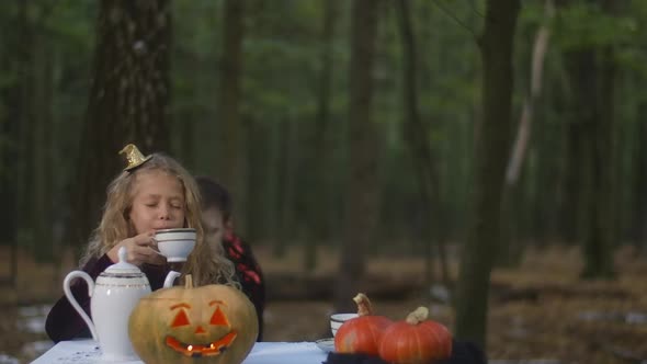 Beautiful Girl Sitting at Table in Forest Drinking Tea As Vampire Scaring Kid alt