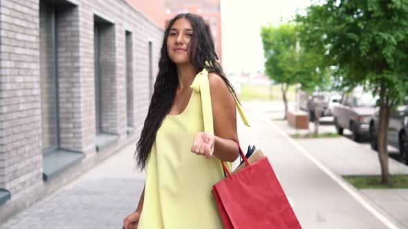 A Beautiful Girl in a Yellow Dress is Walking Down the Street After Shopping alt