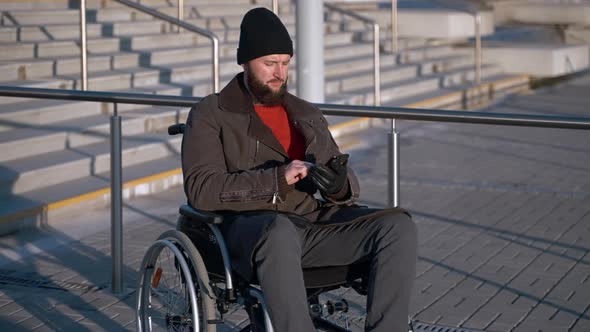 Middleaged Disabled Man is Sending Message By Smartphone Outdoors in City alt
