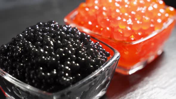 Red and Black Caviar in Two Identical Transparent Glass Bowls on a Black Background alt