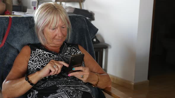 Senior Woman Looking on Mobile Phone Relaxing on Sofa at Home