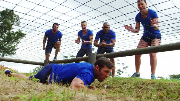 Fit man crawling under the net during obstacle course while fit people cheering 4k alt