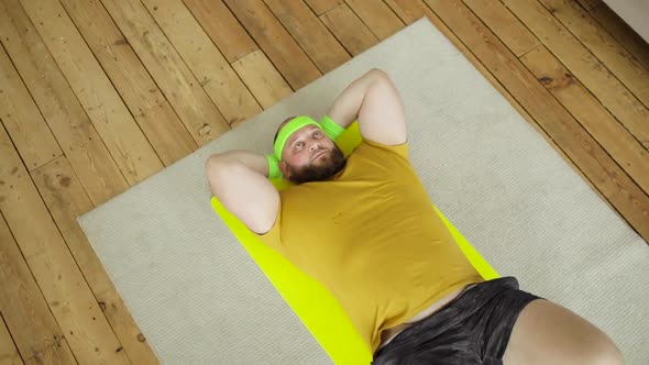 Fat Tired Man in Yellow Sportswear Doing Abs Exercise Crunches Lying on Mat