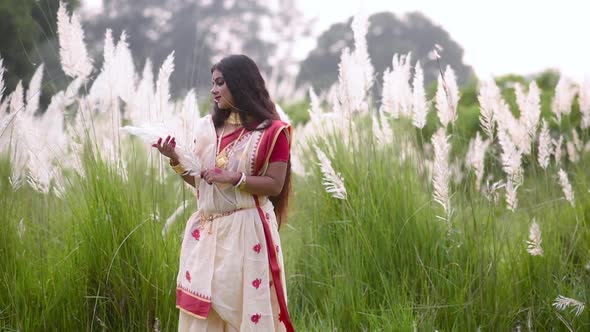 A calm and beautiful Indian woman is happy and plays with white grass called saccharum spontaneum in alt