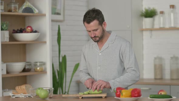 Young Man in Pajamas Peeling Cucumber in Kitchen alt