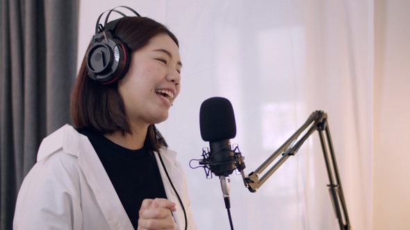 Young Asian female podcaster talking into a microphone while recording a podcast.